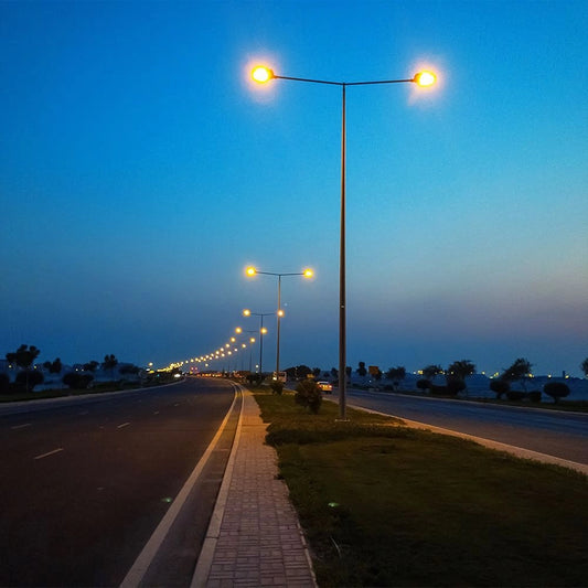 Lampioni stradali con Armature LED 100W V-TAC accese al tramonto, perfette per illuminazione pubblica su strade e viali residenziali.