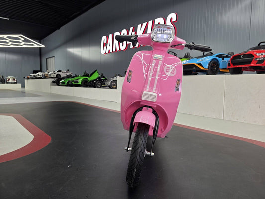 Vista laterale della moto elettrica rosa per bambini con dettagli di design, sedile nero e ruote robuste, in un showroom con auto giocattolo