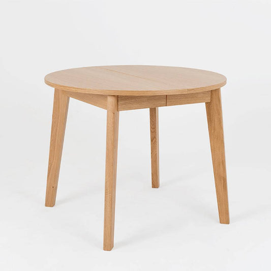 Tavolo in legno di quercia naturale con forma rotonda, gambe inclinate e superficie liscia, perfetto per pranzi conviviali in casa.