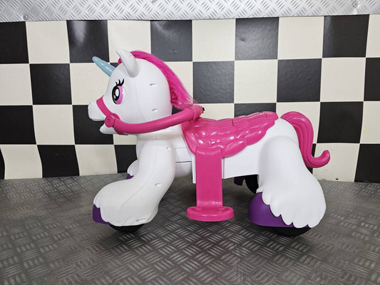 Vista frontale del cavallo a dondolo unicorno bianco con dettagli rosa e corno blu, sedile rosa e ruote nere, su sfondo a scacchi