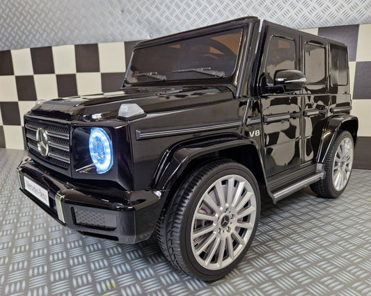 Vista frontale dell'auto elettrica per bambini Mercedes G500 nera metallizzata, con dettagli lucidi, fari LED blu accesi, design realistico e dimensioni compatte