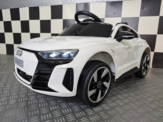 Vista frontale dell'auto per bambini Audi E-Tron bianca con fari LED accesi, dettagli neri, griglia frontale e ruote grandi in plastica