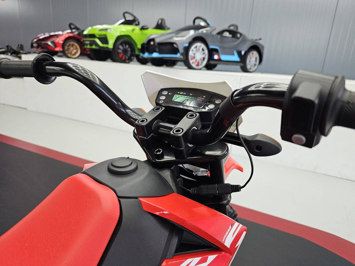 Manubrio di una moto elettrica per bambini con display digitale e comandi, parte anteriore di veicolo rosso e nero, dettagli tecnici visibili