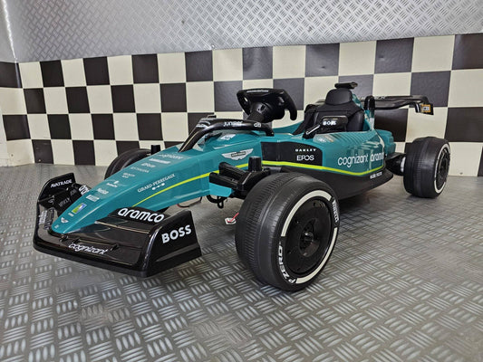 Auto elettrica per bambini Aston Martin F1 24V verde vista frontale, con volante e dettagli di sponsorizzazione, perfetta per giochi all'aperto.
