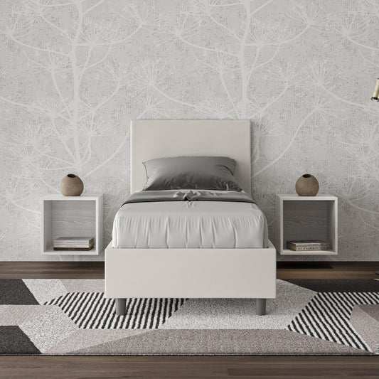 Letto singolo Adele in similpelle bianca con testata imbottita, inserito in una camera moderna con comodini sospesi e tappeto geometrico.