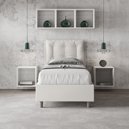 Letto singolo Annalisa bianco in similpelle con testata imbottita, inserito in una camera moderna con mensole e illuminazione sospesa.