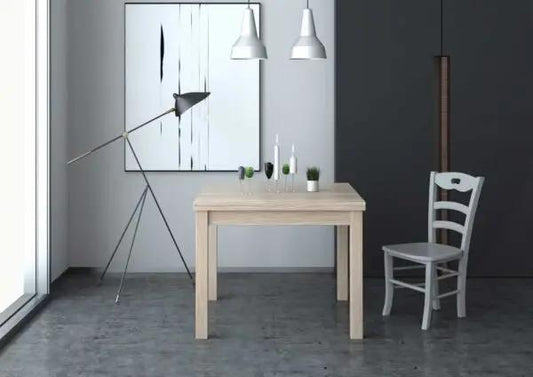 Tavolo allungabile color legno chiaro con gambe in massello e piano nobilitato 110/150x70 cm, in un ambiente moderno con lampada e sedia bianca.