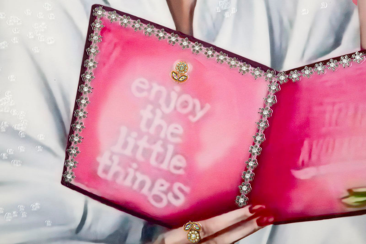 Zoom sul libro rosa con scritta 'enjoy the little things', elemento centrale del dipinto su tela laccato Luxury Spa con cornice.