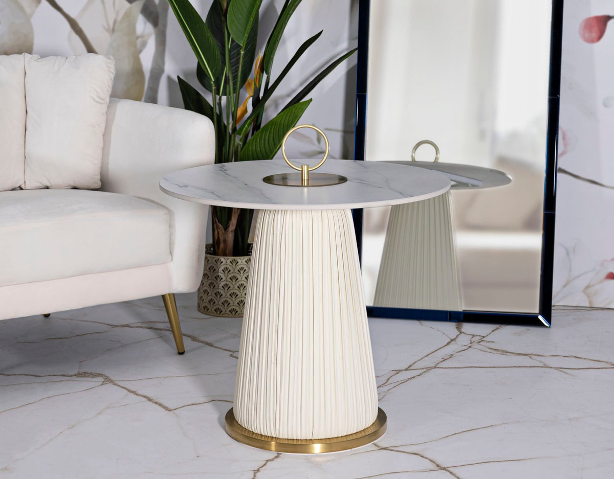 Tavolinetto Nova Ø60x54 cm posizionato in un salotto moderno con divano bianco e piante decorative. Top effetto marmo e base dorata.