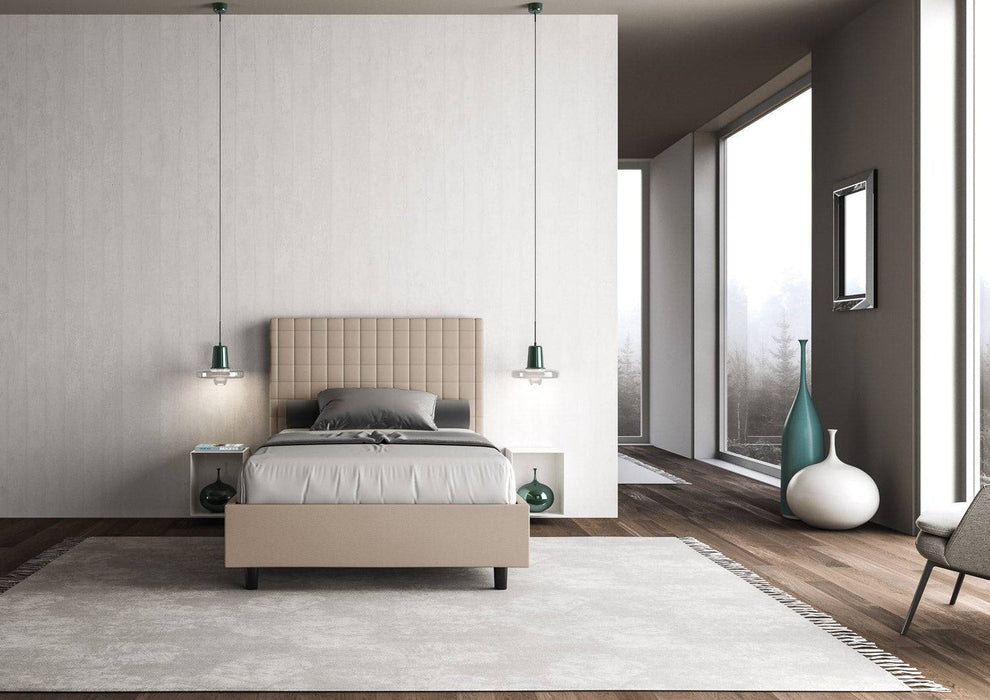 Letto singolo contenitore imbottito similpelle Sunny beige in ambiente elegante con tappeto chiaro e grandi vetrate panoramiche.