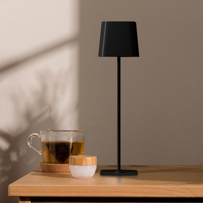 Lampada da tavolo nera moderna con base sottile e paralume a forma di cono, posizionata su un tavolo in un ambiente domestico con luce soffusa