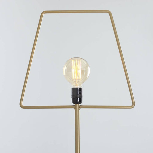 Lampada da terra Firkant Oro con struttura dorata, posizionata su scrivania con oggetti colorati, design contemporaneo e elegante