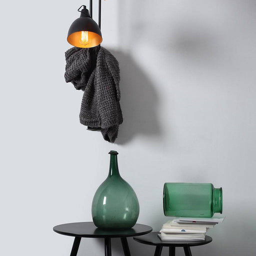 Lampada da parete Coben nera installata su parete bianca, illuminando un ambiente moderno con accessori decorativi come vasi e tessuti