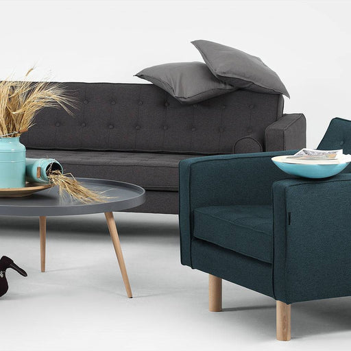 Soggiorno con divano in tessuto grigio scuro, poltrona blu, tavolino rotondo in legno e decorazioni, stile contemporaneo, ambientazione domestica