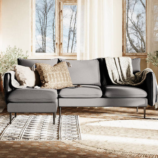 Divano angolare design minimalista in tessuto grigio scuro con cuscini decorativi e tappeto in stile rustico, perfetto per ambienti accoglienti.