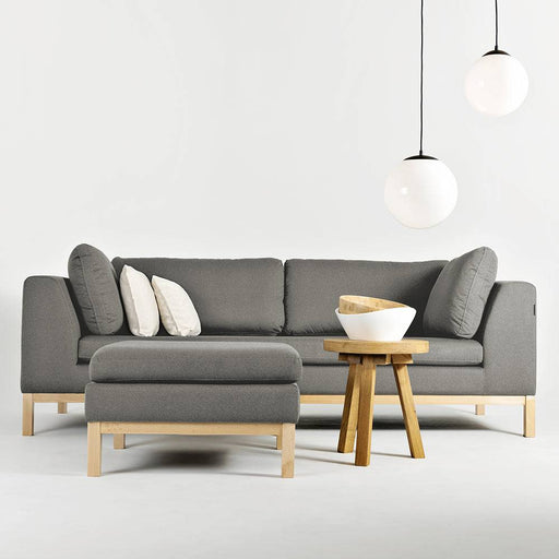 Divano angolare grigio con pouf e tavolino in legno chiaro, stile moderno e accogliente, ideale per soggiorno elegante