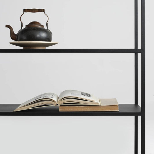 Dettaglio di una libreria nera con ripiano in metallo, decorata con teiera in ceramica e libri, stile minimalista e moderno