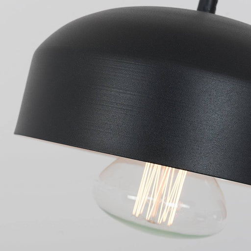 Dettaglio della lampada da soffitto con paralume nero e lampadina a vista, superficie esterna liscia e finitura opaca, stile industriale