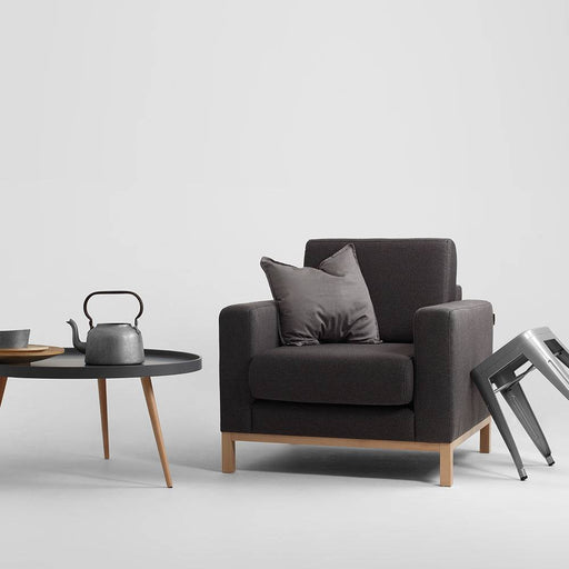 Poltrona SCANDIC in tessuto grigio scuro con dettagli in legno naturale, stile minimalista e comfort elevato, perfetta per ambienti eleganti.