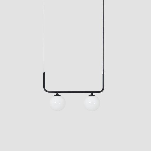 Lampada a sospensione con struttura nera e due globi di vetro bianco opaco, installata sopra un divano grigio in un ambiente minimalista