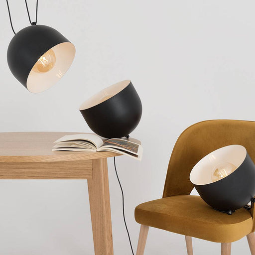 Lampada a soffitto nera con riflettore bianco interno, posizionata sopra tavolo in ambiente moderno, stile minimalista, con cavi a vista