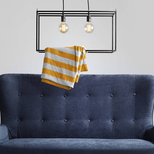 Dettaglio del divano cozyboy in velluto blu navy con schienale imbottito, decorato con lampada a vista e asciugamano giallo e bianco