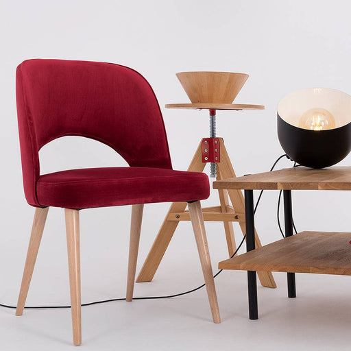 Sedia in velluto rosso con struttura in legno, inserita in ambiente moderno con tavolo in legno e lampade di design