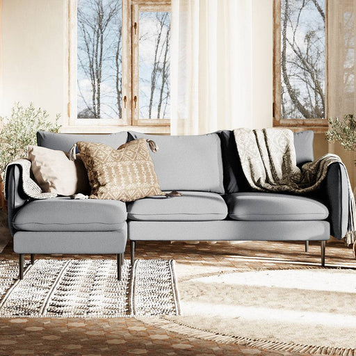 Interno con divano in tessuto grigio chiaro, stile contemporaneo, con cuscini decorativi e pavimento in legno, ambiente accogliente