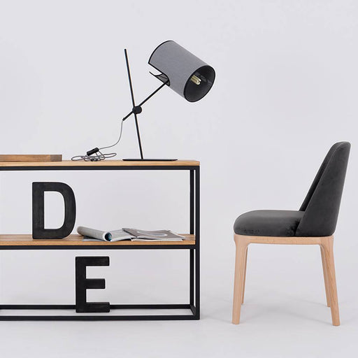 Sedia con rivestimento in velluto nero e struttura in legno naturale, posizionata accanto a una scrivania minimalista in un ambiente di design.