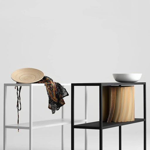 Console in metallo nero con doppio ripiano, stile minimalista, posizionata in un ambiente bianco, con oggetti decorativi e libri