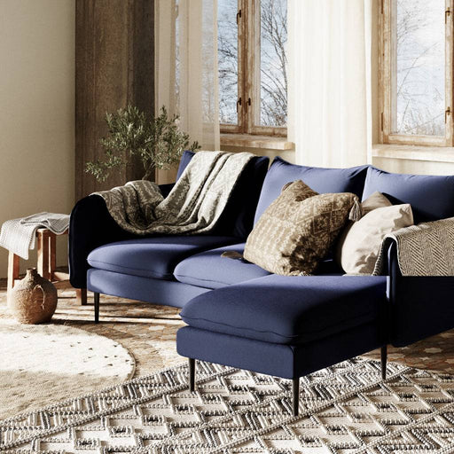 Divano in tessuto inchiostro blu con cuscini decorativi in tonalità neutre, ambientazione accogliente con finestre e decorazioni rustiche