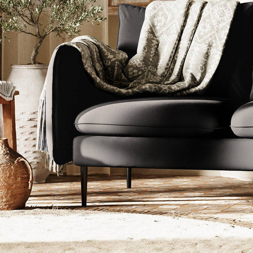 Divano in pelle nera con seduta e schienale imbottiti, decorato con coperte e cuscini beige e con motivi geometrici, in ambiente accogliente.