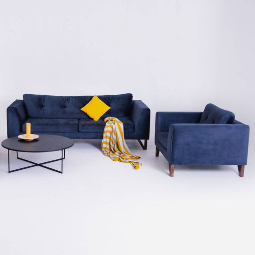 Set di divani in velluto blu scuro con cuscini gialli, tavolino nero rotondo e decorazioni moderne, ideale per soggiorno elegante.