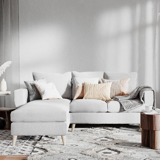 Soggiorno con divano in tessuto grigio chiaro, decorato con cuscini color crema e beige, in ambiente luminoso e elegante