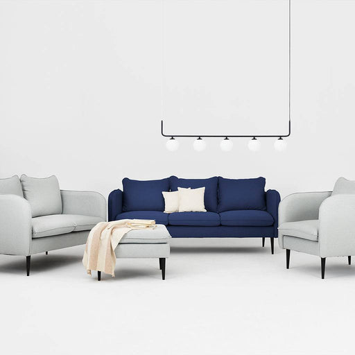 Divano blu inchiostro con rivestimento in tessuto, accompagnato da pouf coordinato e sedie bianche in un ambiente minimalista.