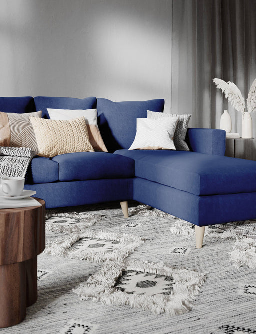 Dettaglio del divano angolare in tessuto inchiostro con cuscini decorativi color crema e grigio, ambiente moderno con pareti bianche e pavimento in legno