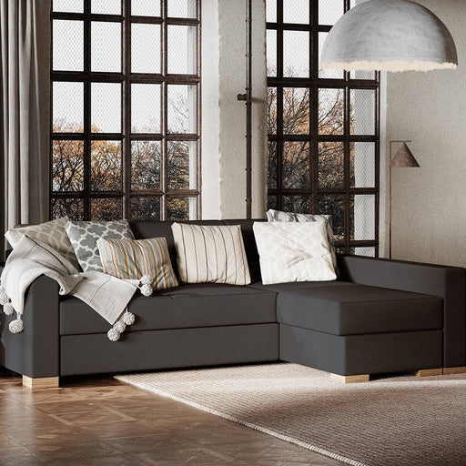 Divano grigio scuro con seduta spaziosa e cuscini decorativi, in ambiente con grandi finestre e pavimento in parquet, stile contemporaneo.