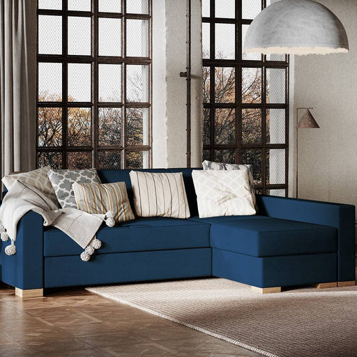 Soggiorno con divano angolare blu Chokeberry, rivestimento in tessuto, decorato con cuscini, in ambiente luminoso con grandi finestre.