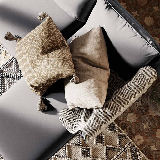 Immagine di cuscini decorativi in tessuto beige e pattern geometrici, disposti su divano con rivestimento in tessuto grigio chiaro.