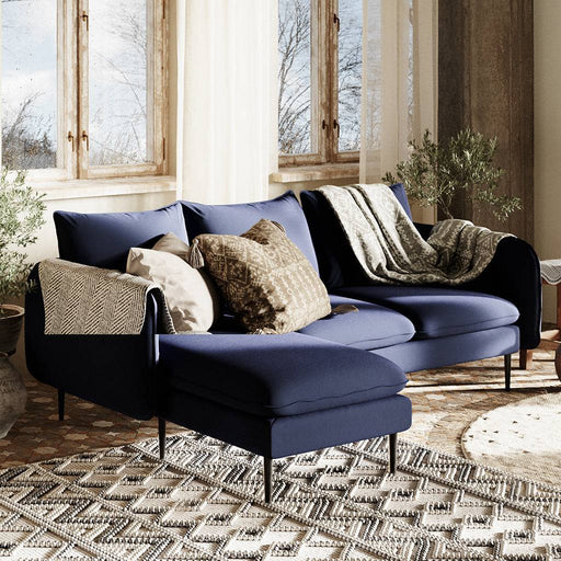Divano ad angolo moderno in inchiostro, rivestimento in tessuto blu scuro, con cuscini decorativi in tonalità neutre, ambiente luminoso e accogliente