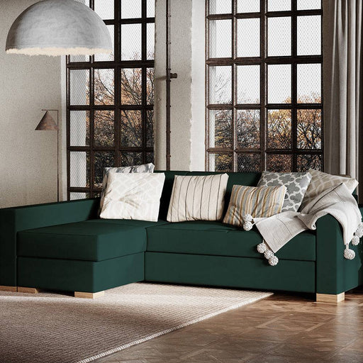 Soggiorno con divano angolare in tessuto verde scuro, ampio e confortevole, decorato con cuscini colorati e illuminato da grandi finestre.