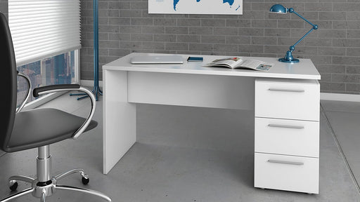 Scrivania bianco lucido con 3 cassetti, posizionata in un ufficio moderno con sedia ergonomica e lampada da tavolo. Dimensioni 138x60x74 cm.