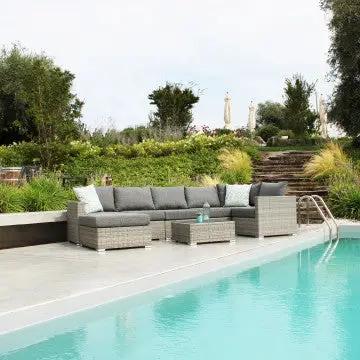 Set da giardino con divano angolare e Tavolino Copacabana in wicker grigio, ideale per relax all'aperto vicino alla piscina.