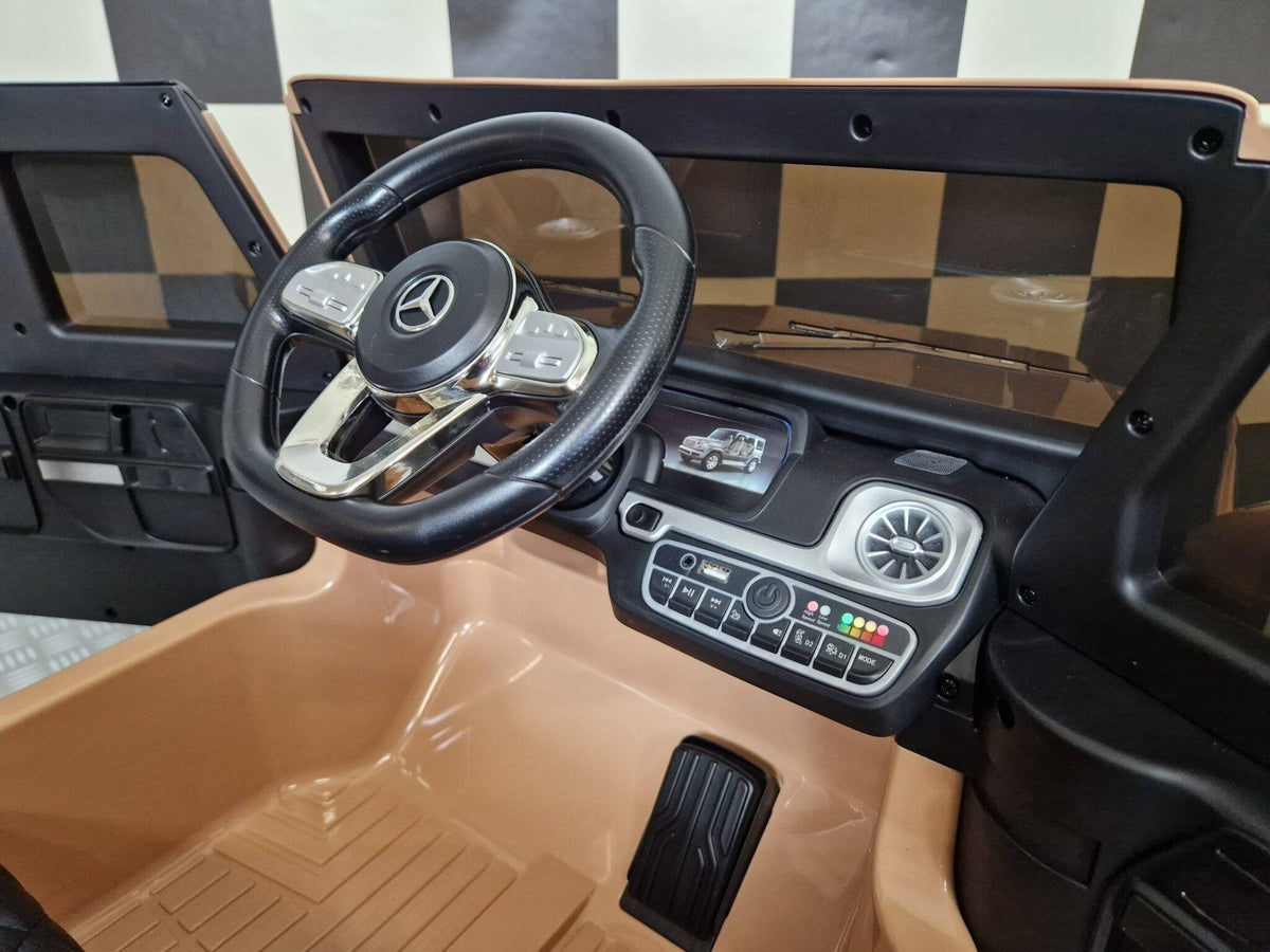 Dettaglio del cruscotto e del volante dell'auto elettrica per bambini Mercedes G500, con pulsanti, luci LED e finiture di alta qualità.