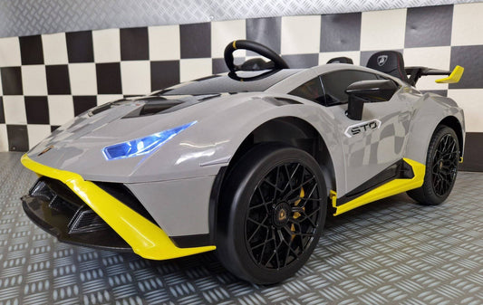 Vista frontale dell'auto elettrica per bambini Lamborghini Huracan STO 12 V grigia con fari LED blu, dettagli aerodinamici e volante sportivo.