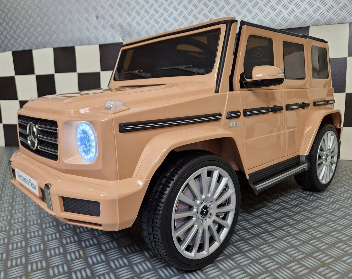 Vista frontale dell'auto elettrica per bambini Mercedes G500 color sabbia con dettagli realistici e luci LED accese
