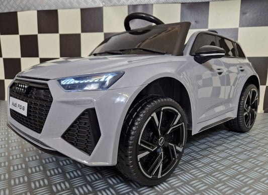 Vista frontale dell'auto elettrica per bambini Audi RS 6 in grigio Nardo, con fari LED accesi, griglia anteriore dettagliata e logo Audi