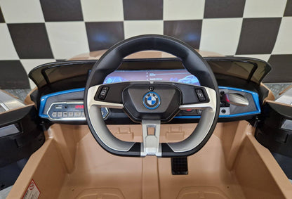 Dettaglio del volante dell'auto elettrica per bambini BMW i4, con logo BMW e comandi integrati, in colore champagne