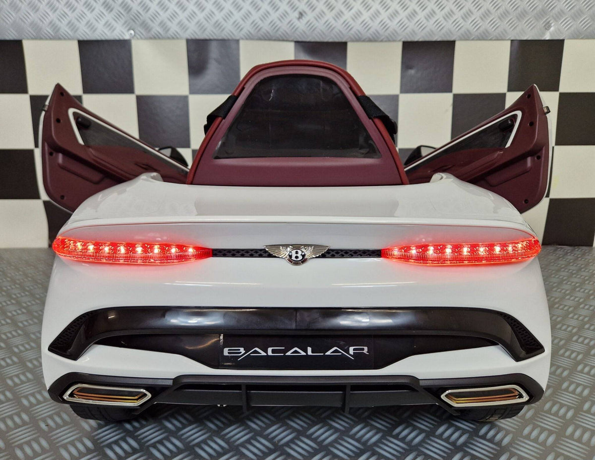 Auto elettrica per bambini Bentley Bacalar bianca con portiere aperte, dettagli realistici e luci posteriori accese, in ambiente con pavimento a scacchi.