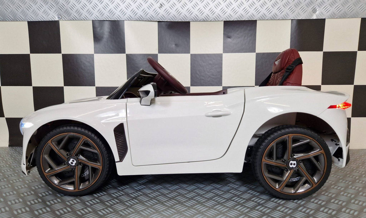 Vista laterale dell'auto elettrica per bambini Bentley Bacalar bianca con dettagli in marrone, sedile rosso e luci accese, stile realistico e sportivo